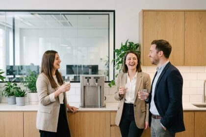 Trois collègues autour d'une fontaine à eau pétillante et plate dans une cuisine de bureau moderne