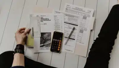 person holding paper near pen and calculator