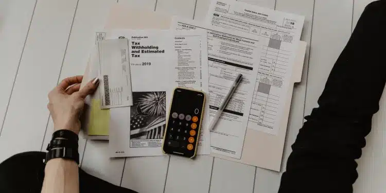 person holding paper near pen and calculator